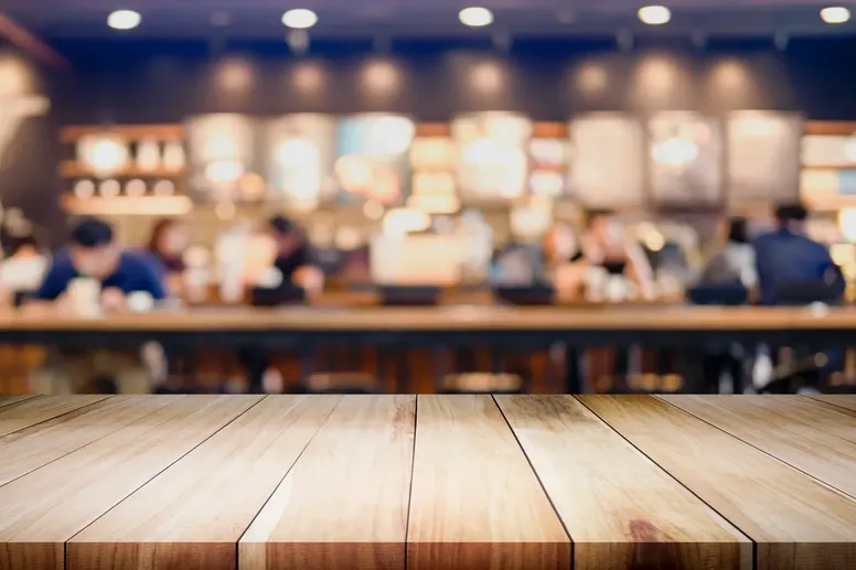 Blurry café background with an empty wooden table in focus, representing The William Stanley Group’s announcement feature in Tampa Bay Business and Wealth.