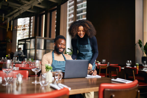 Smiling business owners in a restaurant reviewing financials on a laptop, symbolizing strategic decision-making with break-even analysis tools
