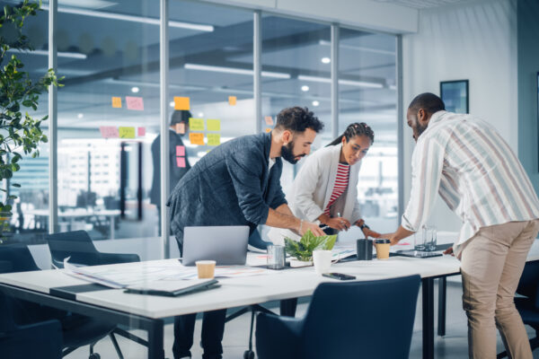 Diverse professionals collaborating around a conference table with post-it notes in the background, illustrating The William Stanley Group’s Teamhood feature on cross-functional team strategies.
