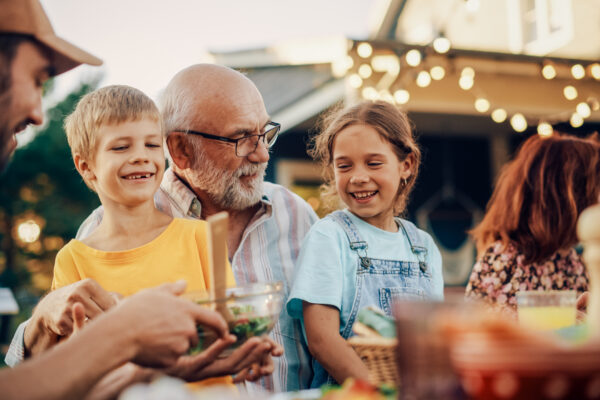 Multigenerational family smiling and sharing food at an outdoor gathering, representing The William Stanley Group’s Go Banking Rates feature on smart financial planning across life stages.