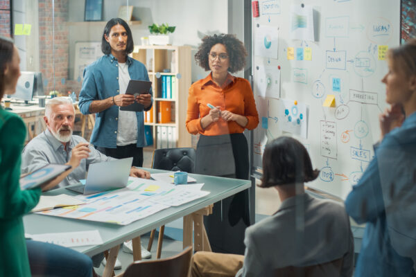 Team of diverse professionals in a collaborative workspace with whiteboards and planning materials, representing The William Stanley Group’s Yahoo Finance feature on the 7-Day Rule.