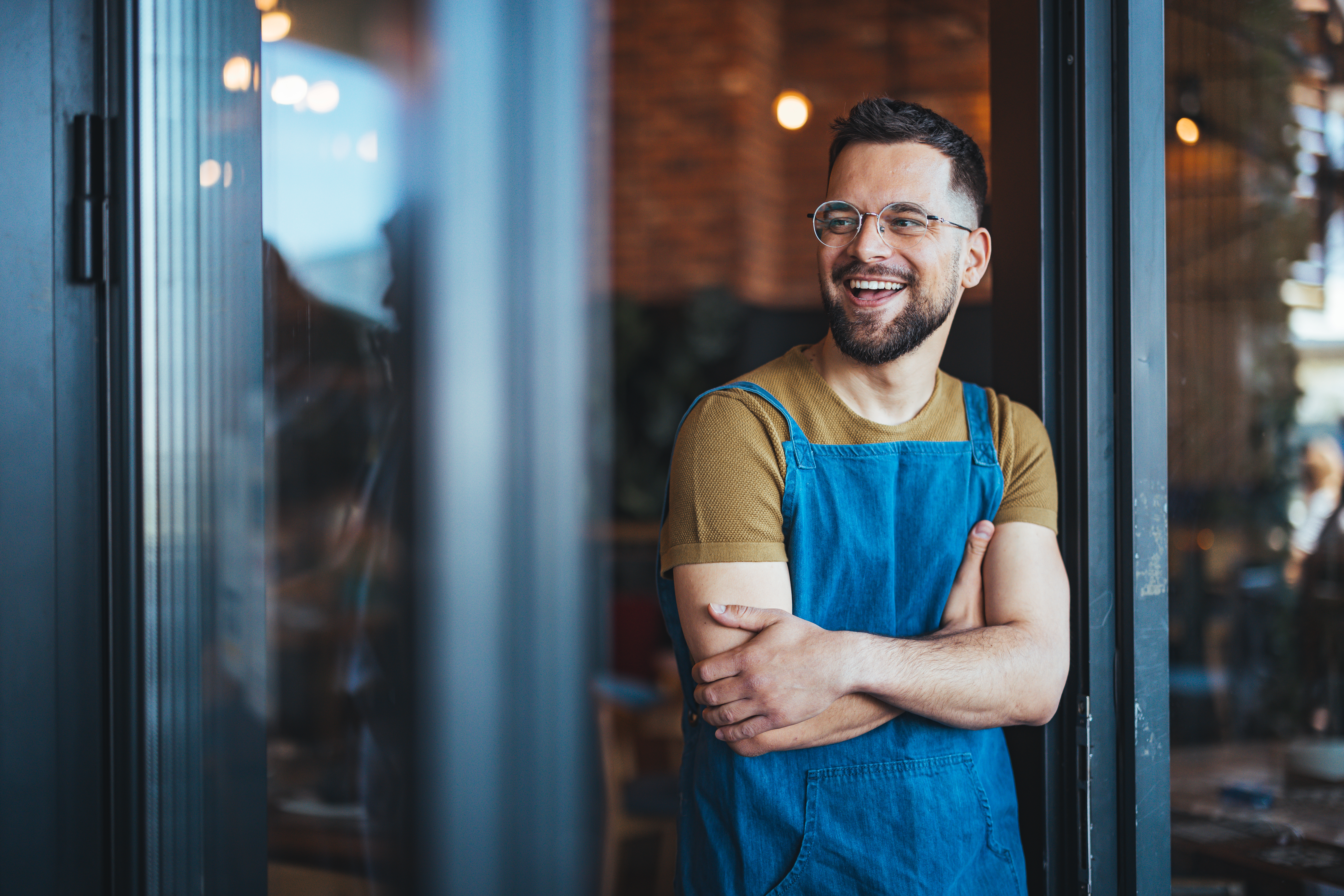 Confident small business owner standing at the entrance of his shop with arms crossed, representing financial preparedness and clarity through Days Cash on Hand forecasting