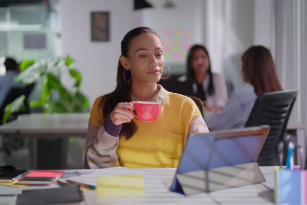 Professional woman sipping coffee while reviewing a tablet in a modern office, reflecting The William Stanley Group’s quote on AI in banking.
