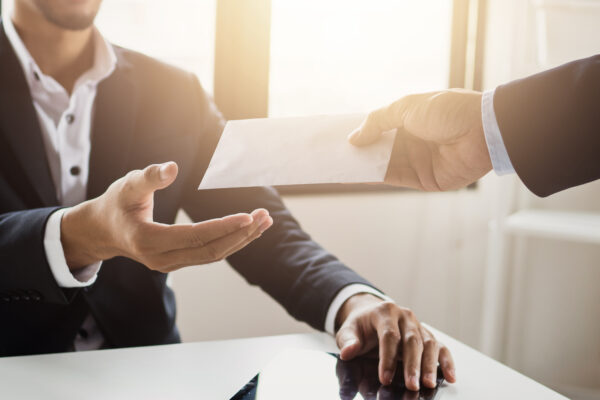 Close-up of a businessperson handing a document across a desk, representing The William Stanley Group’s Think Money feature on quantifying soft savings in business decisions.