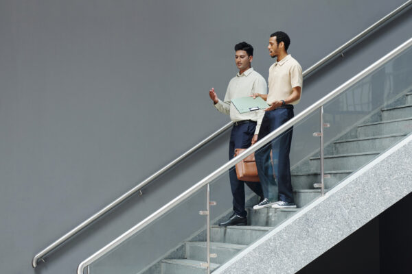 Two professionals walking down a stairwell in conversation, symbolizing The William Stanley Group’s GOBankingRates feature on financial steps after a holiday layoff.