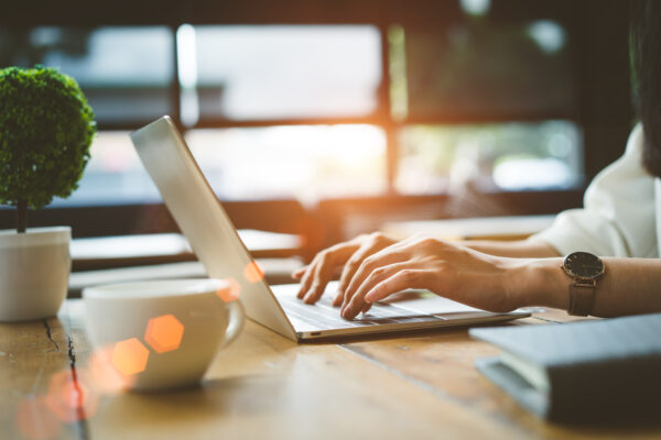 Person typing on a laptop at a sunlit desk, with coffee and notes—reading The William Stanley Group’s business blog for actionable financial insights